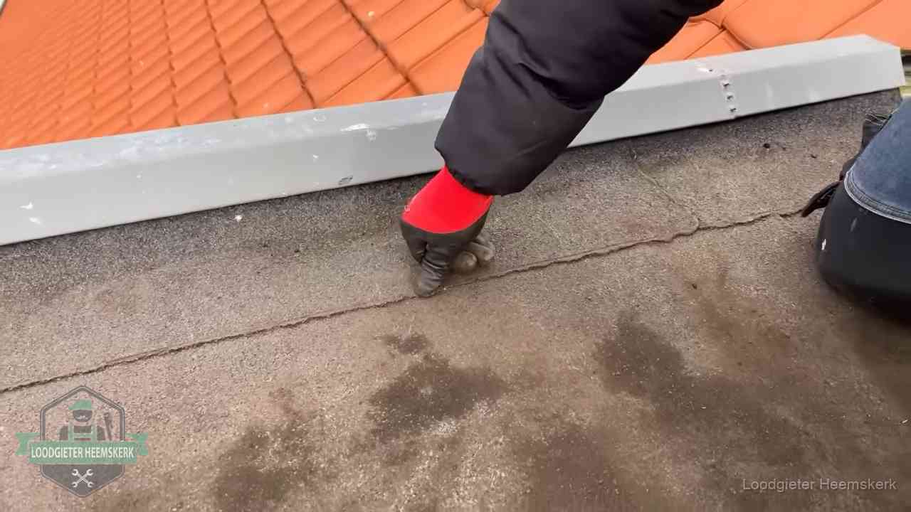 Vakman wijst een naad met vochtplekken aan op een bitumen plat dak in Heemskerk