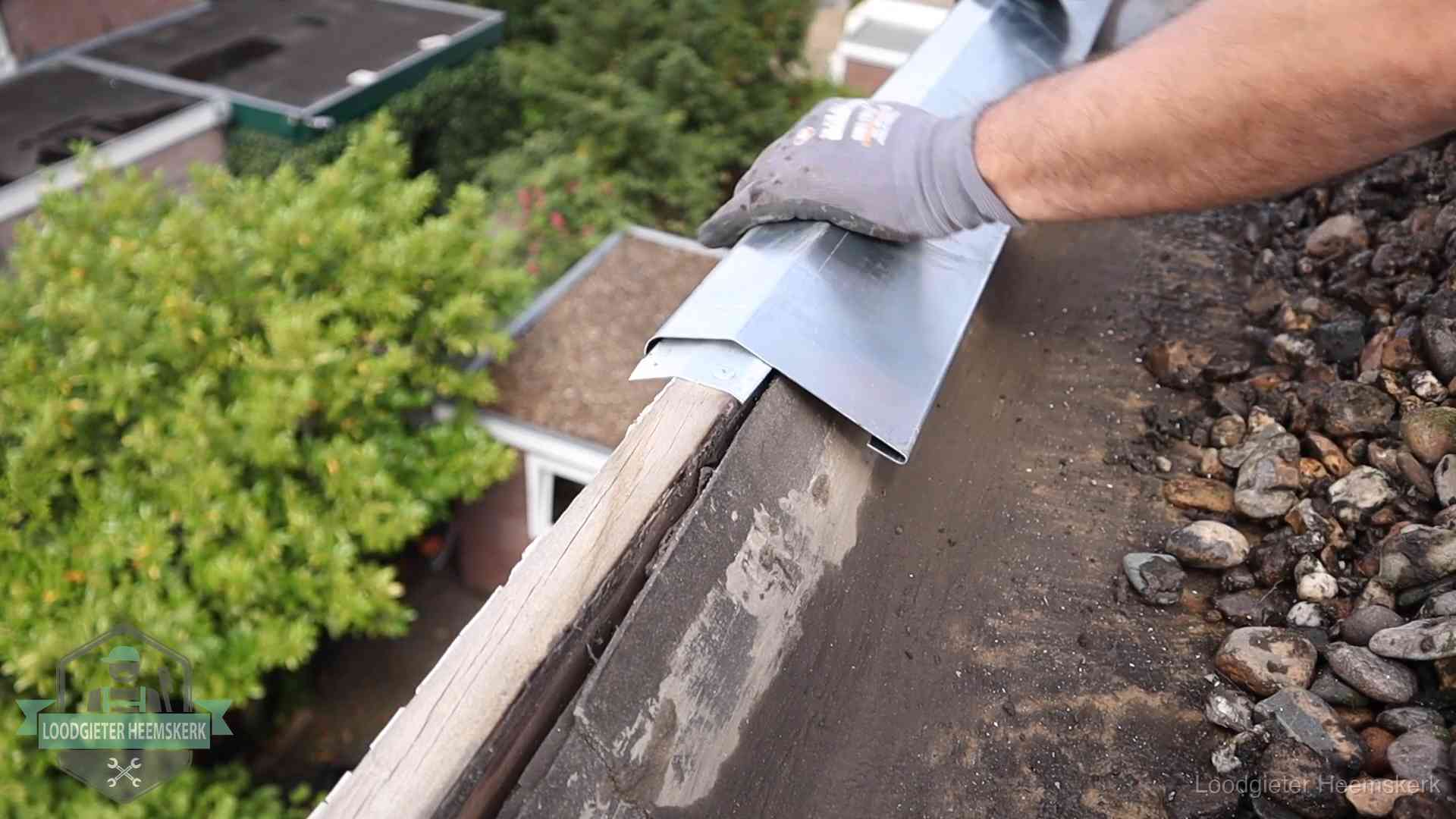 Dakdekker plaatst een zinken deklijst op een dakrand met uitzicht over een woonwijk in Heemskerk