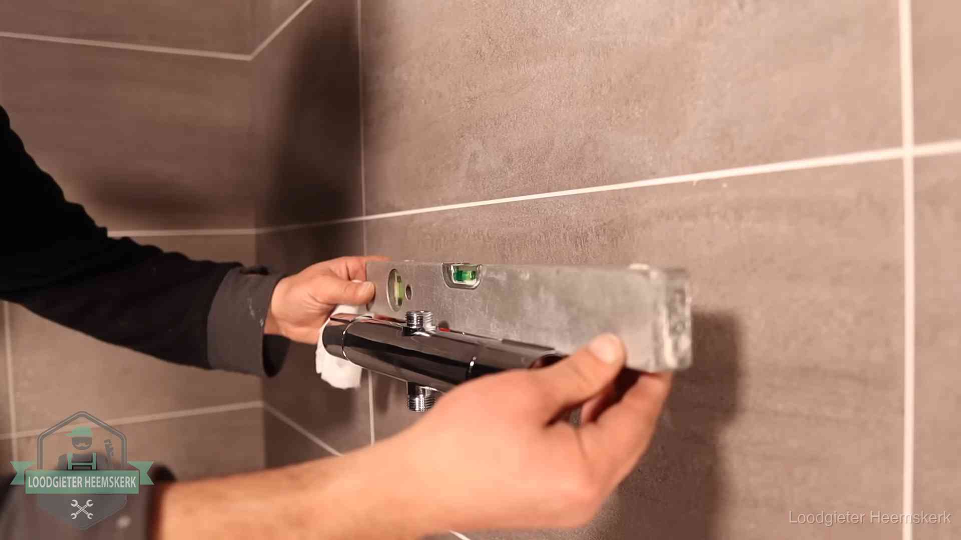 Loodgieter lijnt een douchekraan uit met een waterpas in een woning in Heemskerk