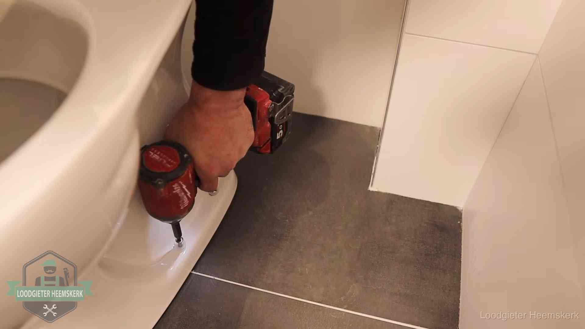 Kosten wc ontstoppen in Heemskerk Loodgieter zet de voet van een wc-pot vast op de tegelvloer in Heemskerk